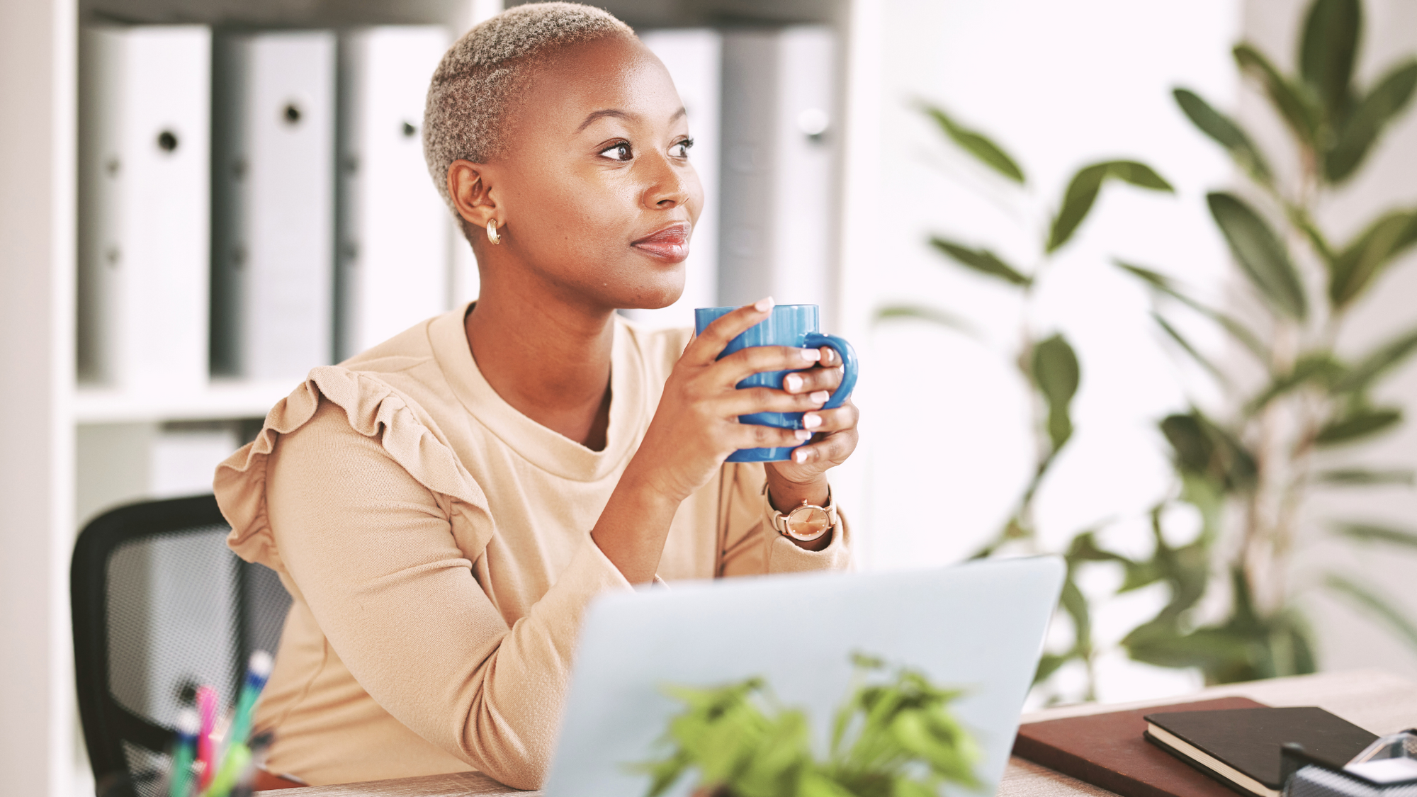 Woman of color drinking coffee in an office. 
